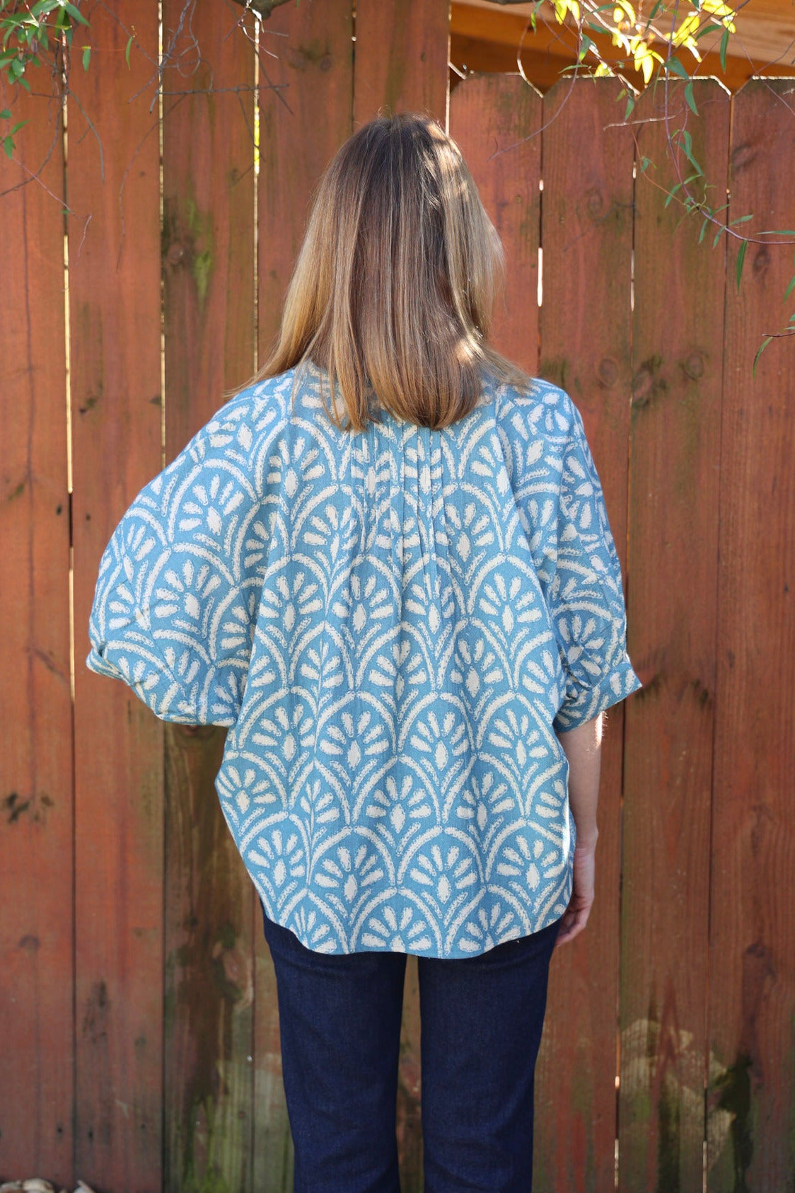 Person wearing a blue patterned shirt standing in front of a wooden fence.