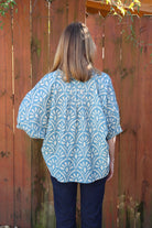 Person wearing a blue patterned shirt standing in front of a wooden fence.